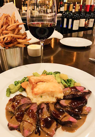Steak with sauce, potato gratin, vegetables, fries, and red wine on a table.