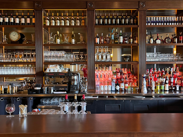 Bar interior with dark wood shelving stocked with bottles and glasses. Stainless steel bar, coffee machine.