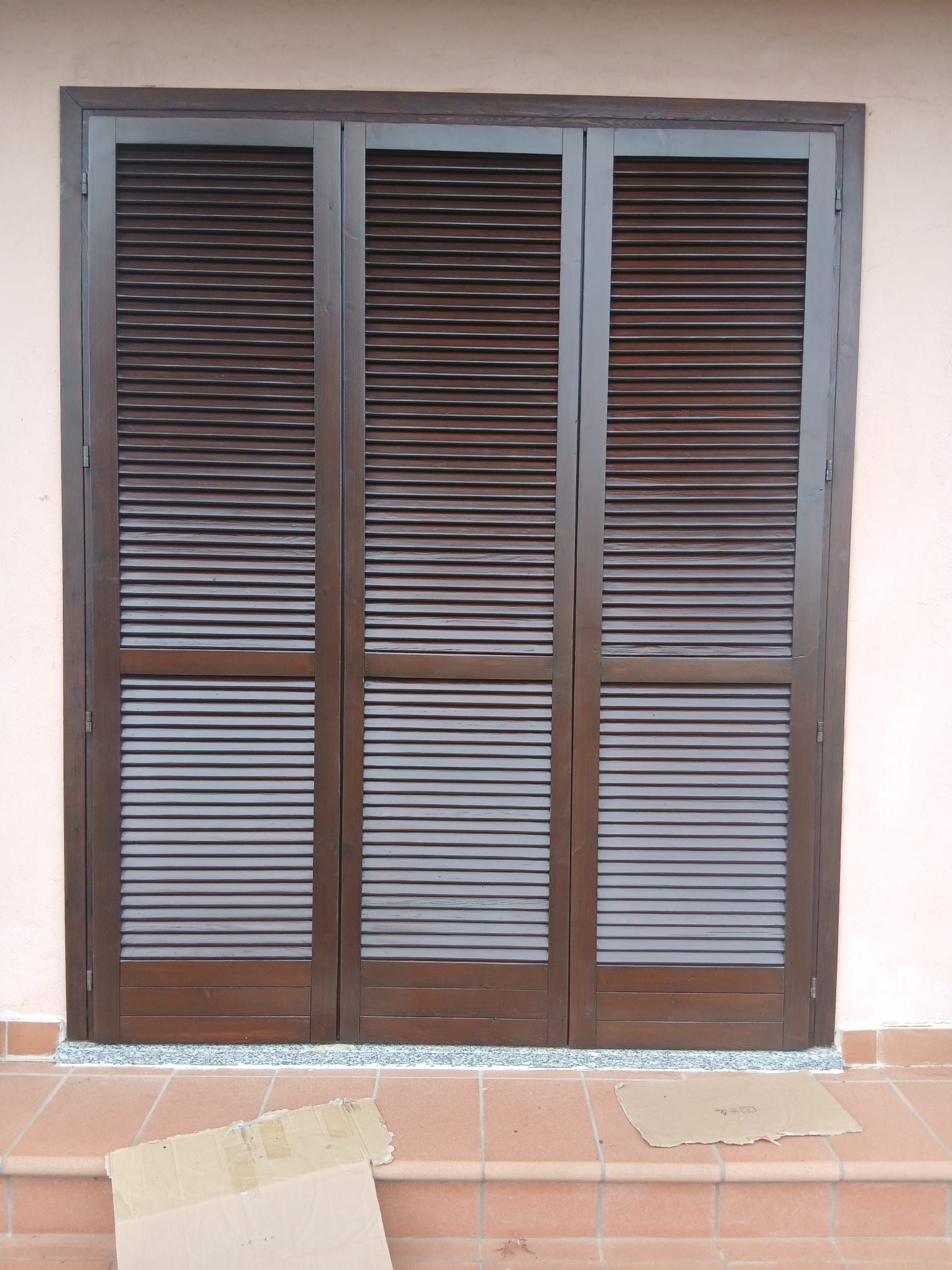 Persiane marroni su una porta, incastonate in una parete di colore chiaro.