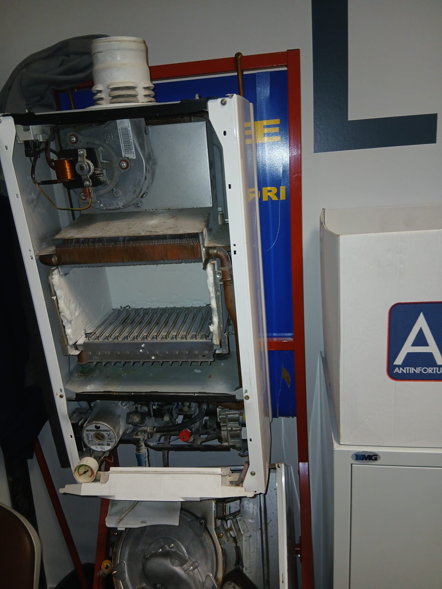 Caldaia a gas aperta con componenti interni visibili. Sono visibili il mobiletto bianco in metallo, le prese d'aria e i comandi del gas.