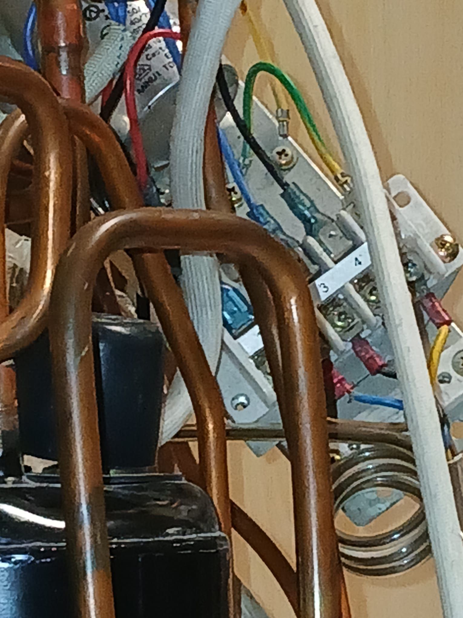 Primo piano dei componenti elettrici, tra cui tubi di rame, fili e morsettiere.