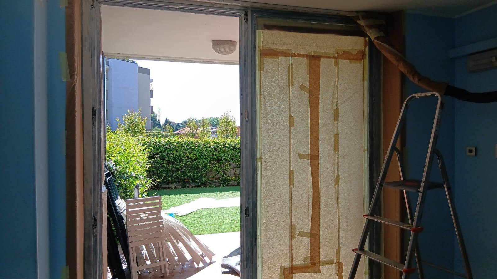 Vista interna del telaio di una porta con isolamento e scala, che si apre su un cortile con erba verde e alberi.