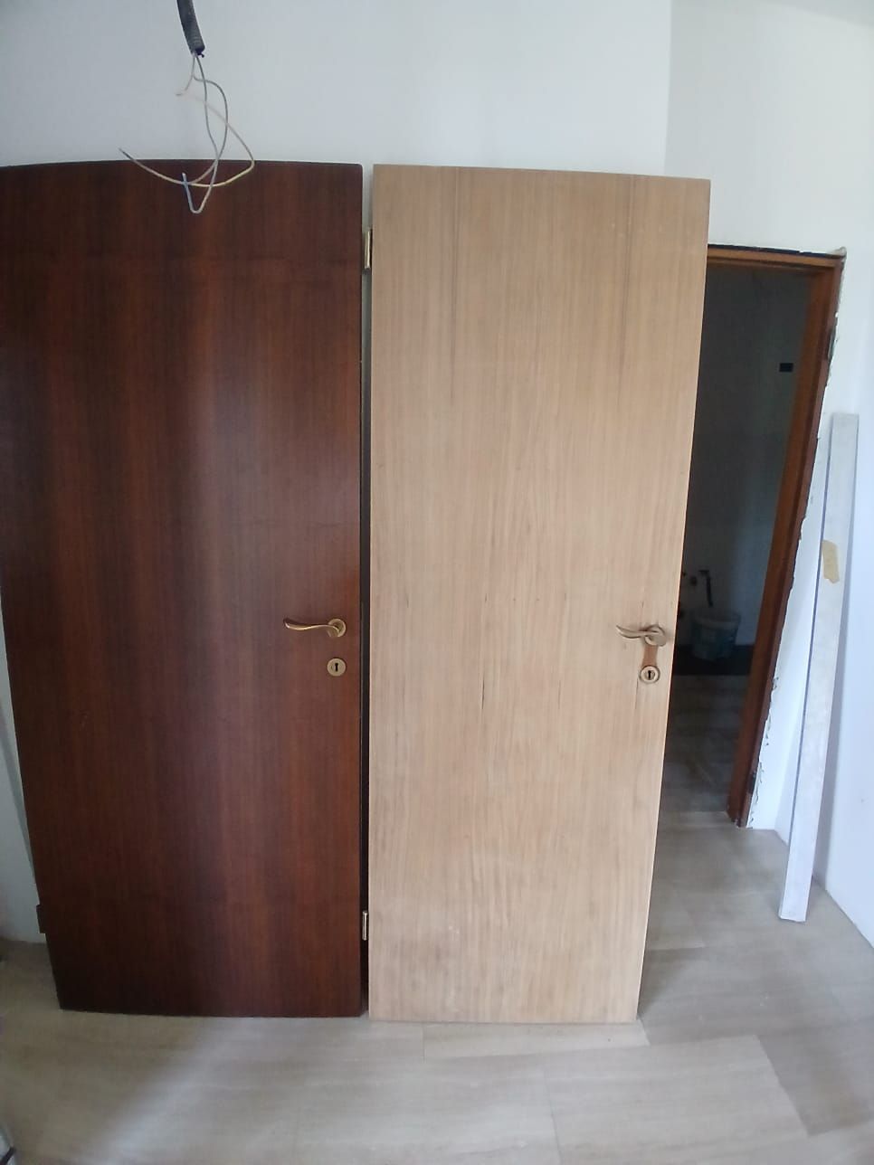 Due porte, una marrone scuro, l'altra chiara, appoggiate a un muro. Una terza porta è aperta sullo sfondo.