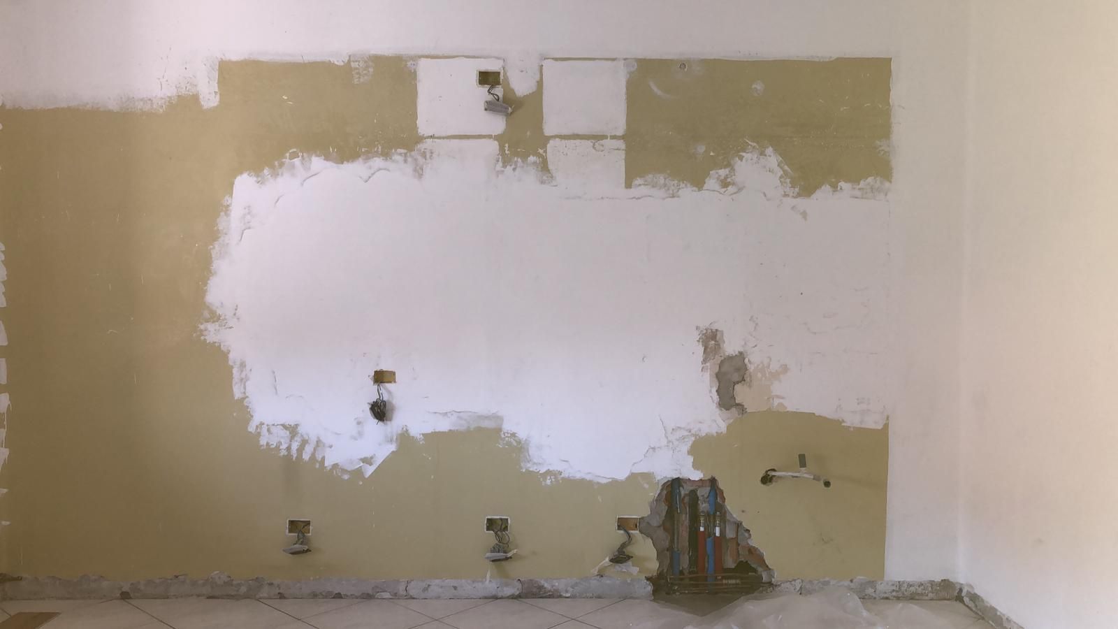 Parete con macchie di vernice di vari colori, che mostrano impianti elettrici e idraulici; ristrutturazione in corso.