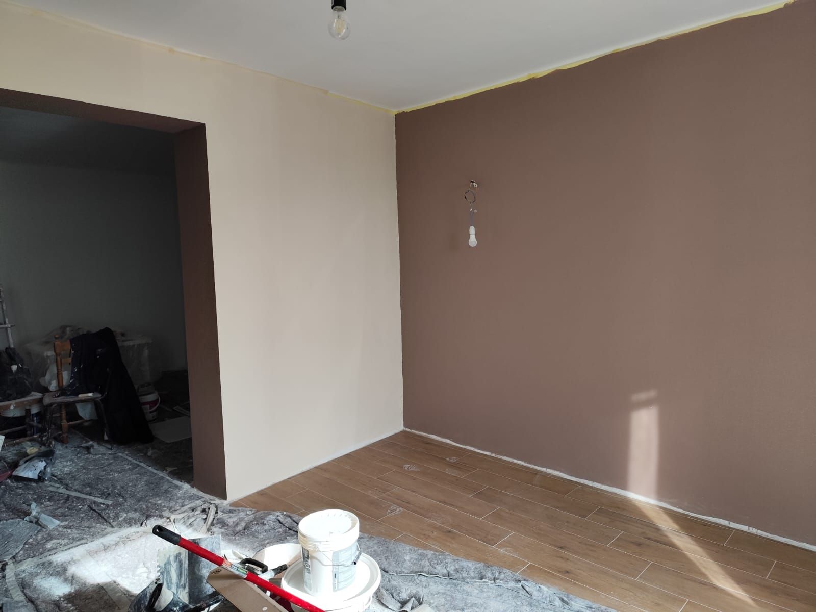 Stanza con pareti, porta e pavimento in legno dipinti di marrone e beige; detriti edili in primo piano.