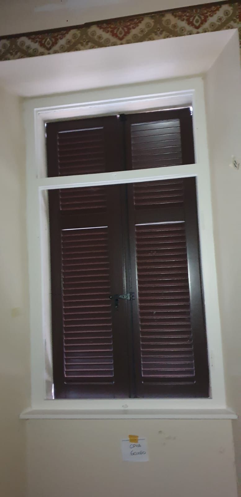 Una finestra con persiane marroni chiuse, inserite in una cornice bianca, all'interno di una stanza.