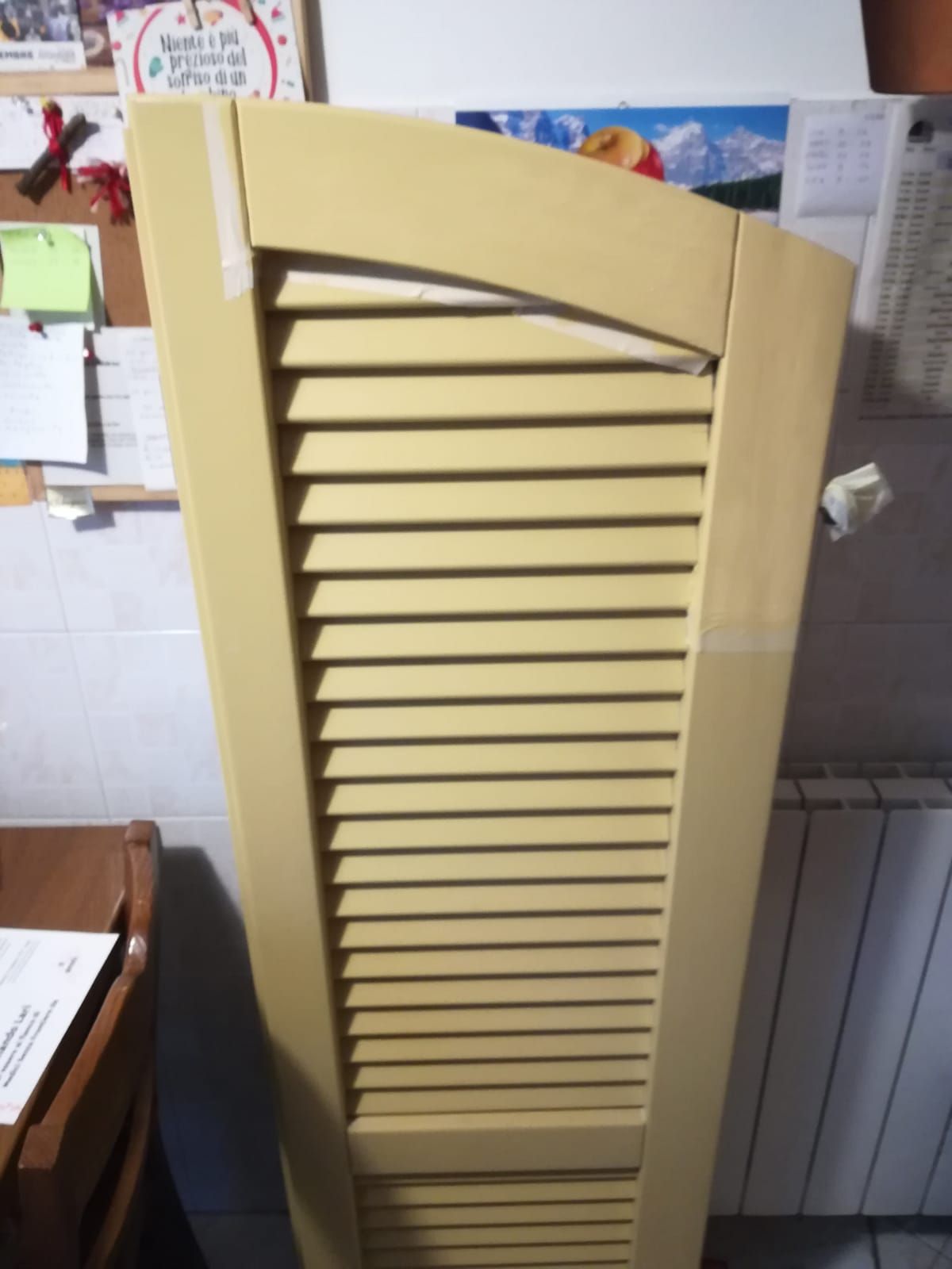 Persiana beige con listelli, fissata con nastro adesivo ai bordi, appoggiata contro un muro.