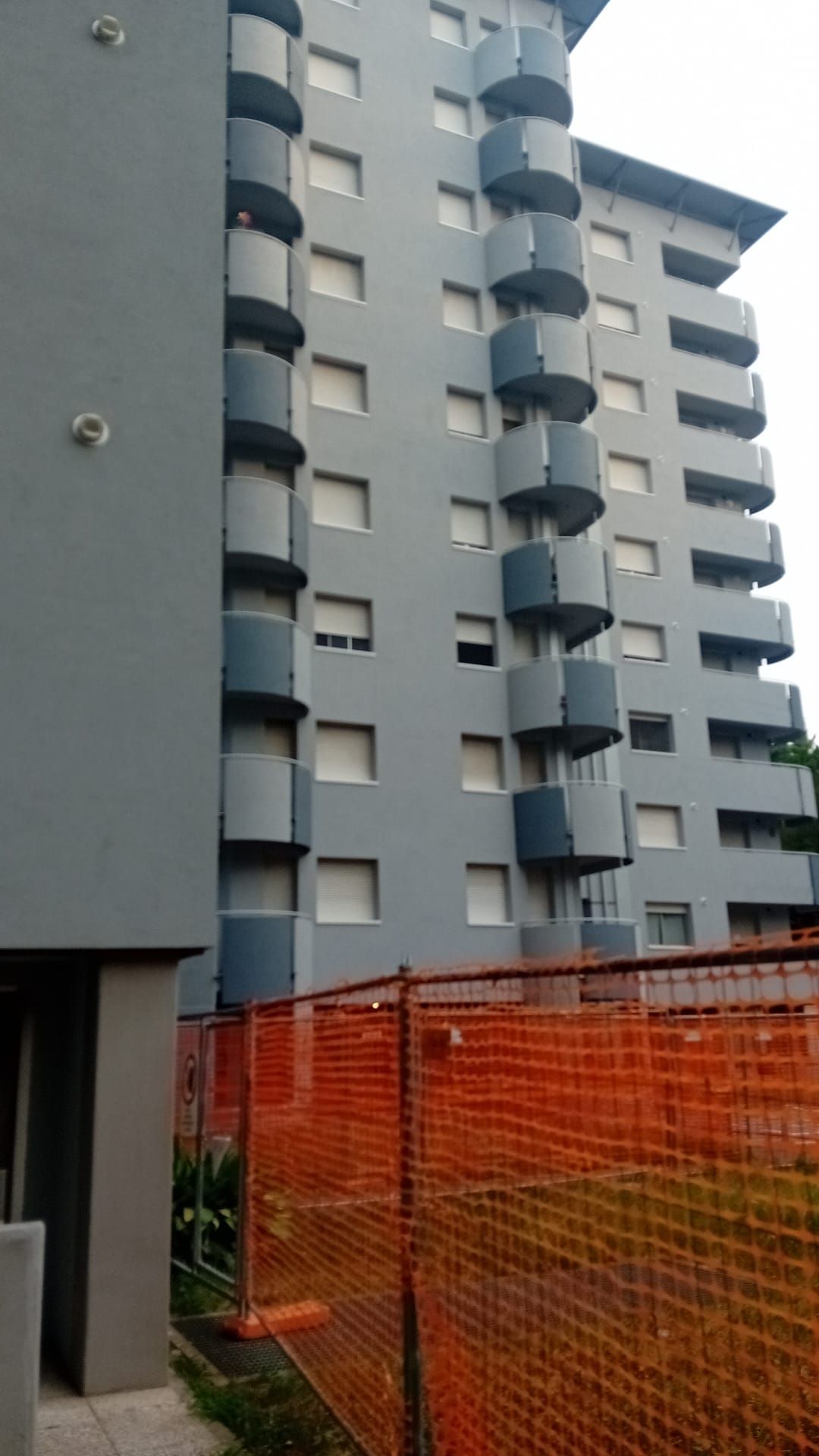 Edificio grigio con balconi cilindrici. Recinzione arancione in primo piano.