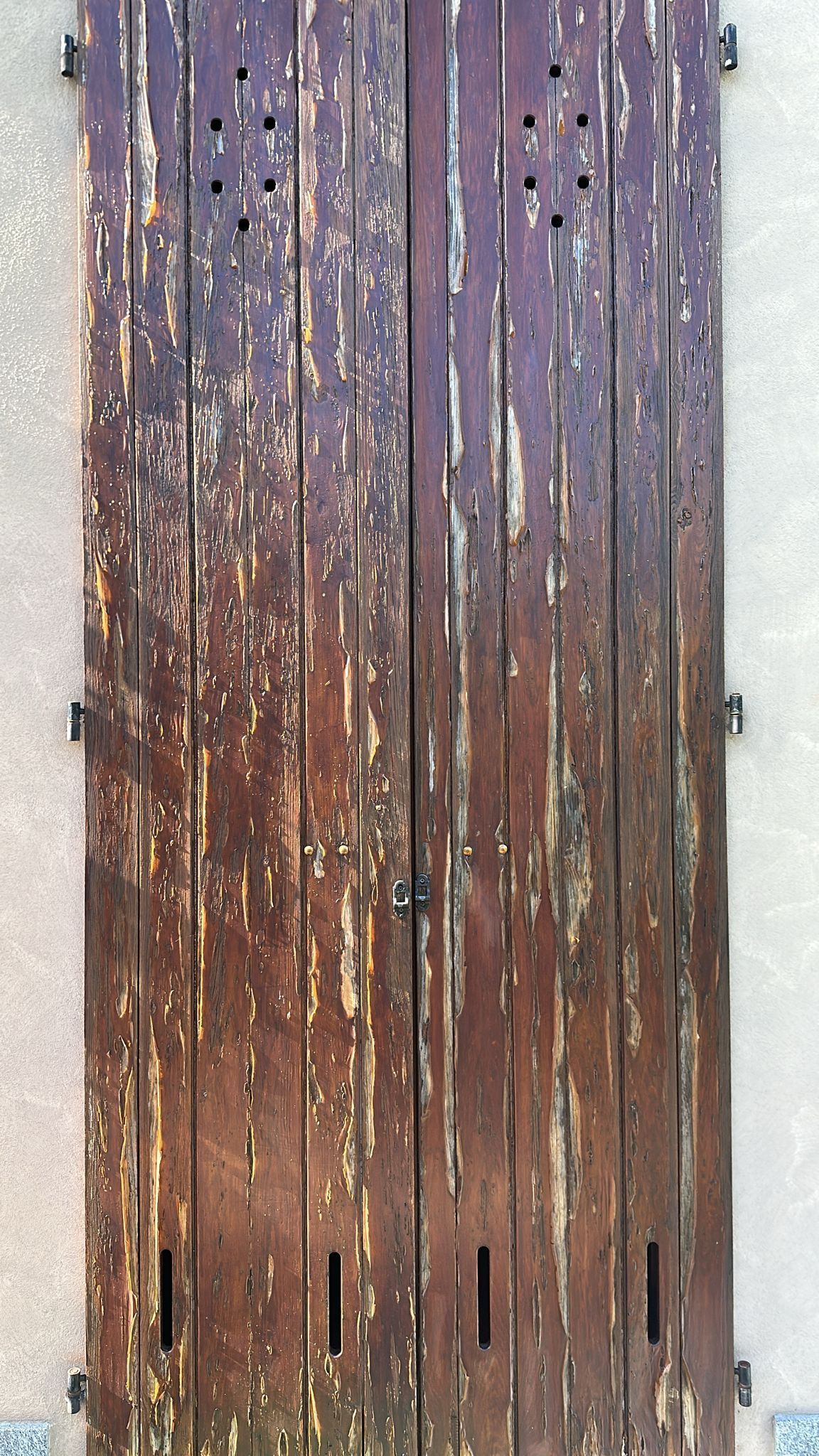 Persiane in legno marrone invecchiato su una parete chiara, con listelli verticali e ferramenta in metallo.