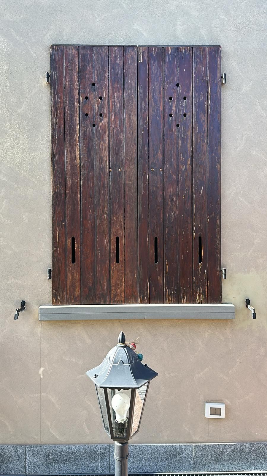 Persiane in legno chiuse su una parete beige sopra una lampada.