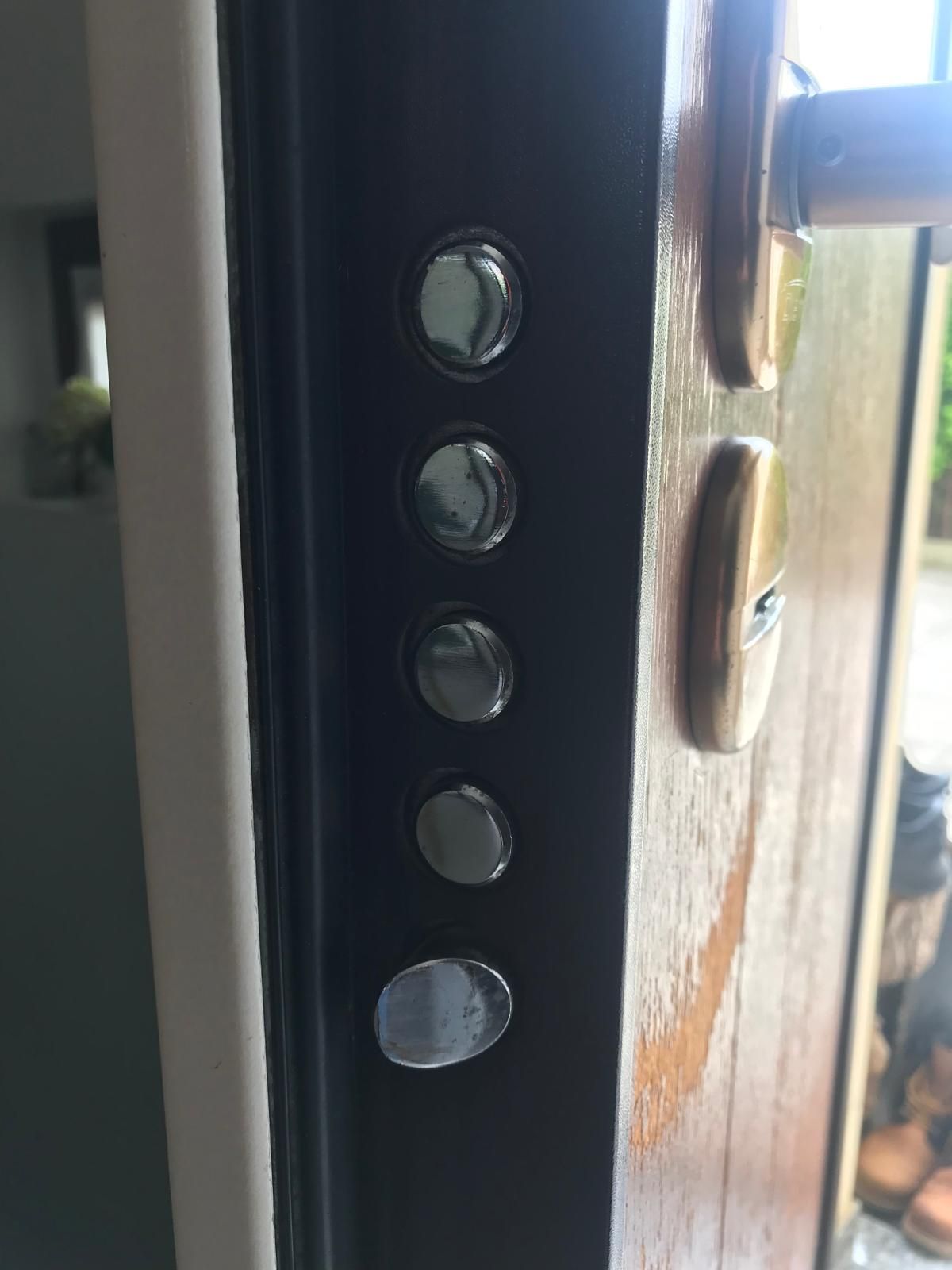 Primo piano del telaio di una porta in acciaio con cinque chiavistelli e una maniglia dorata.