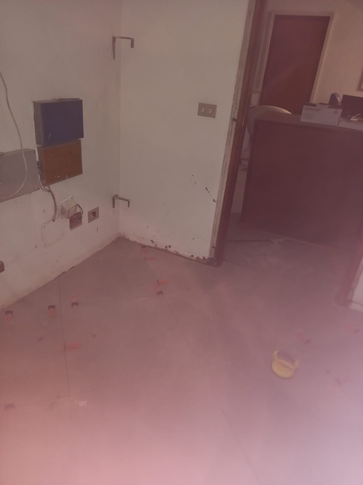 Stanza vuota con cavi elettrici scoperti, angolo con segni sul muro, porta visibile.