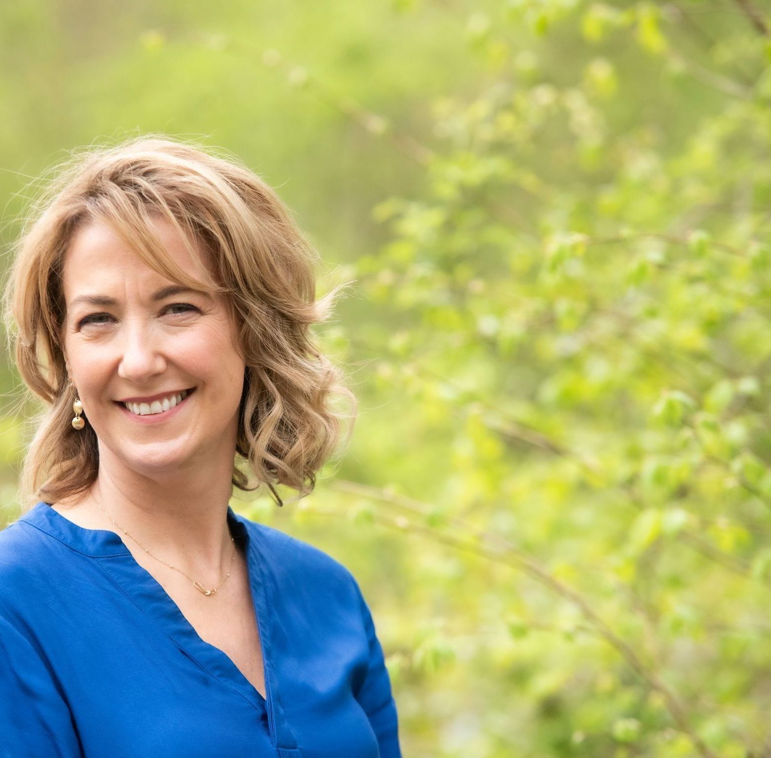 A woman in a blue shirt is smiling for the camera.