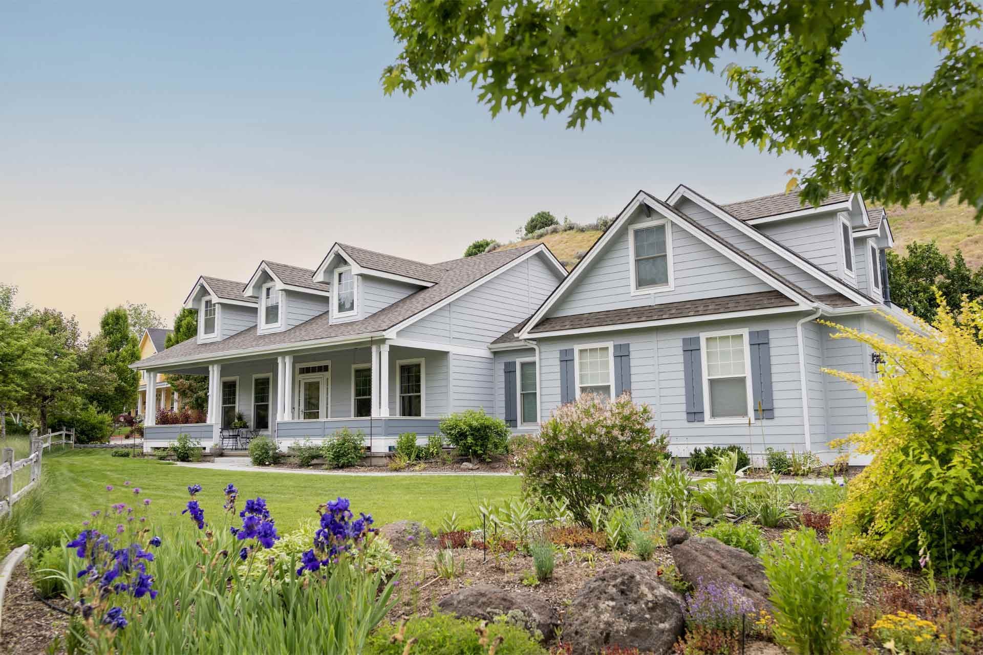 A Large White House With A Large Porch And Flowers In Front Of It — Dayton, OH — Sharp Edge Landscaping And Lawncare LLC