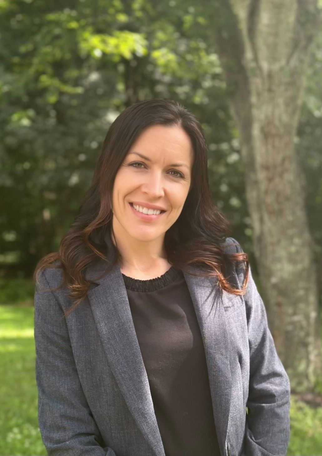 A woman in a gray jacket and black shirt is smiling for the camera.