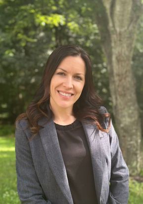 A woman in a gray jacket and black shirt is smiling for the camera.