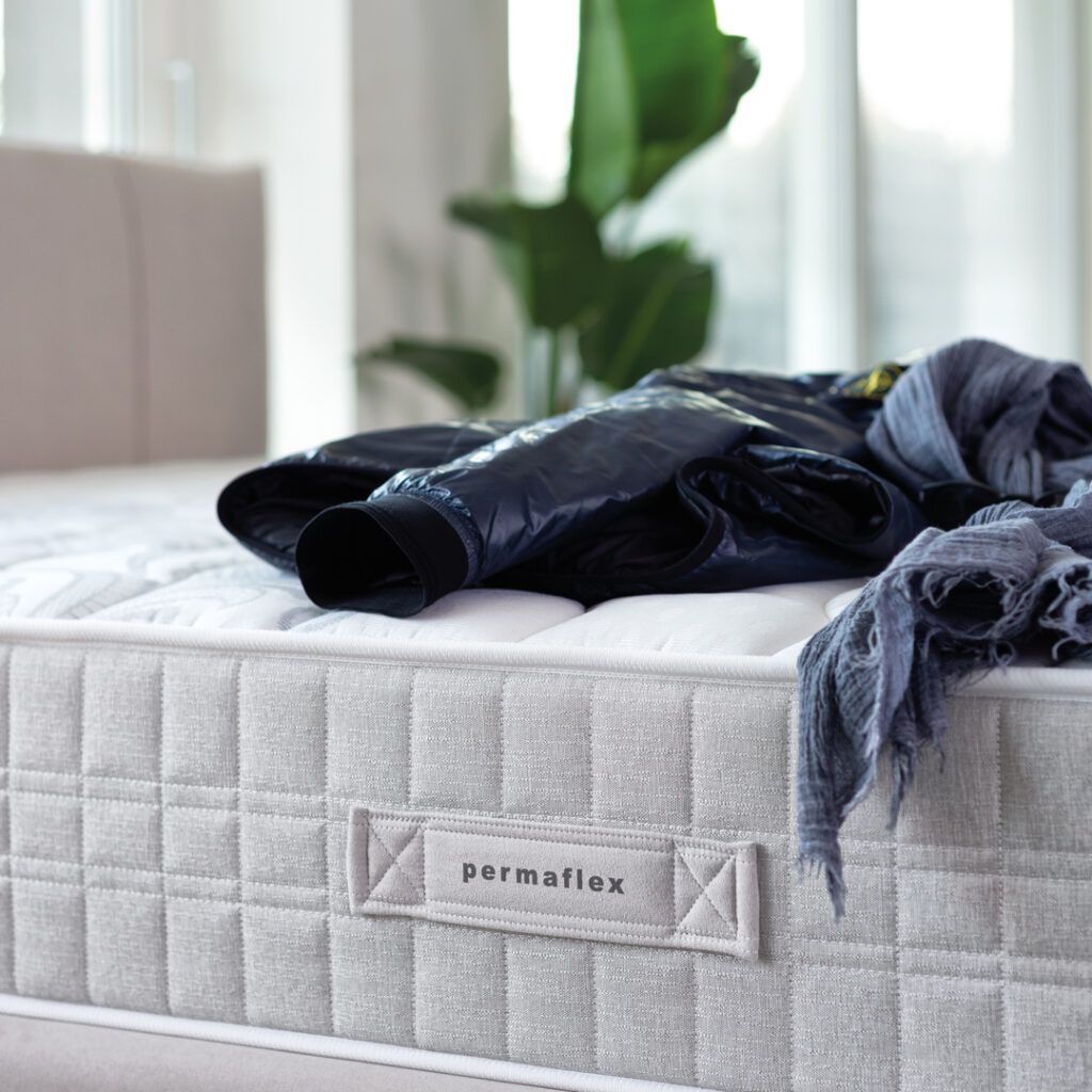 Primo piano di un materasso grigio chiaro con una giacca e una sciarpa appoggiate sopra. È visibile il marchio