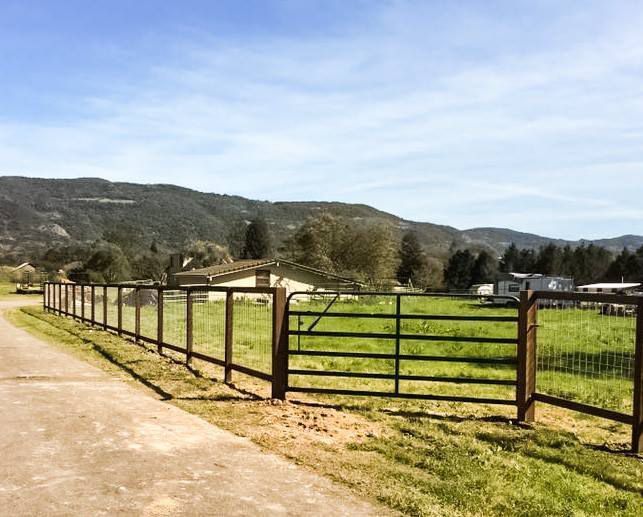 A fence surrounds a grassy field with mountains in the background.