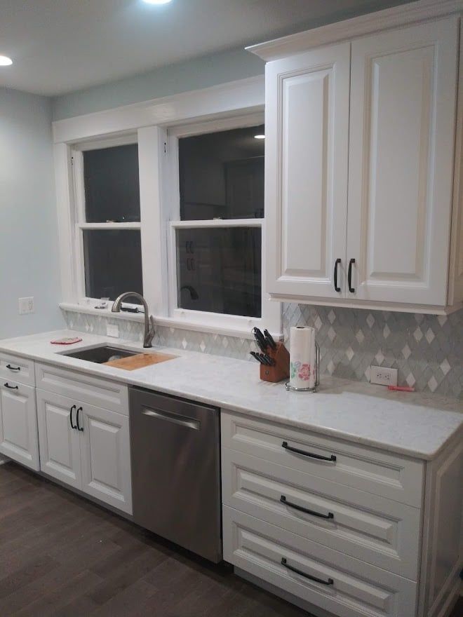 A kitchen with white cabinets , a sink , and a stainless steel dishwasher.
