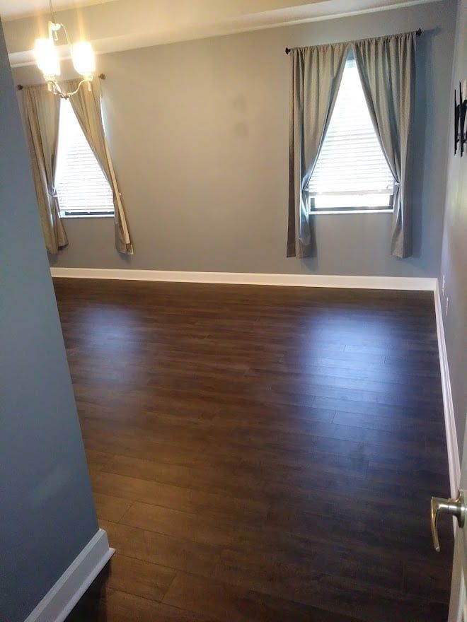 An empty living room with hardwood floors and two windows.