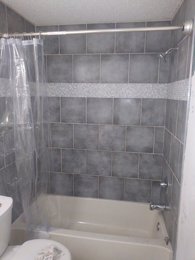 A bathroom with a tub , toilet , shower and tiled walls.