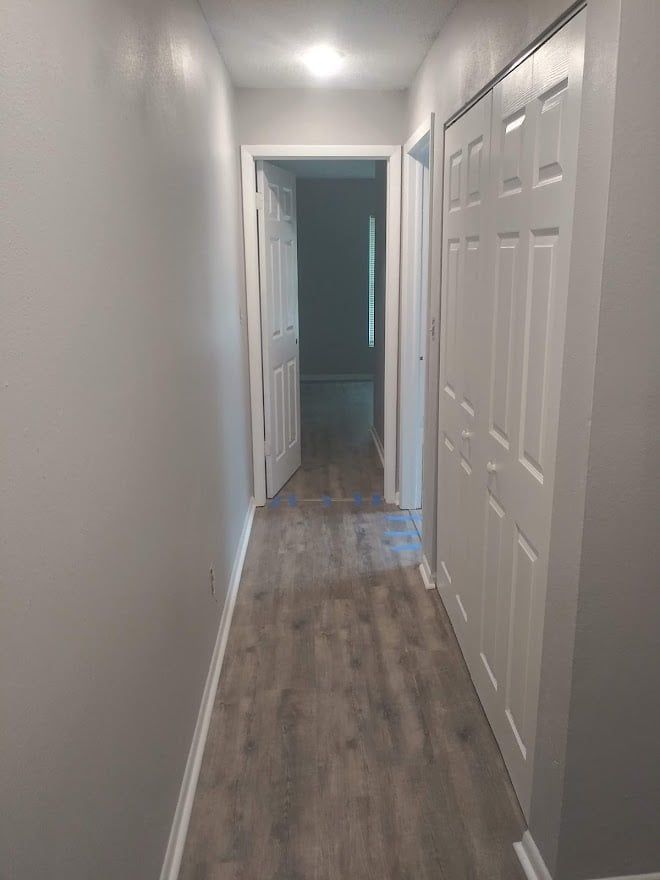A long hallway with hardwood floors and white doors leading to a bedroom.