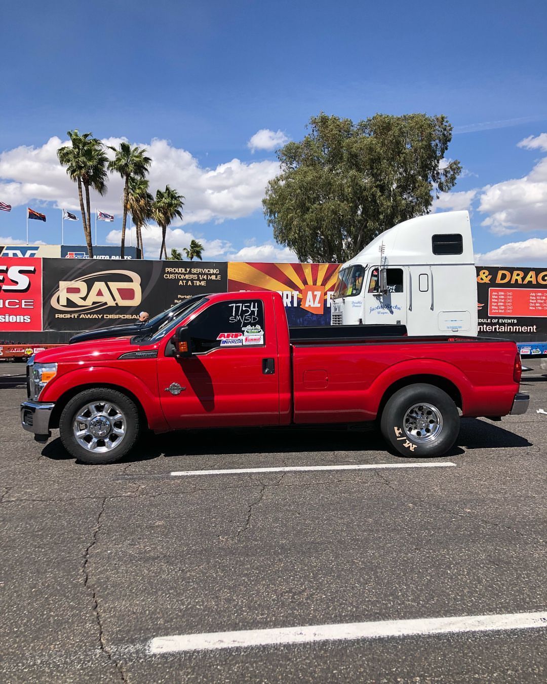 A red truck is parked in a parking lot in front of a sign that says rad