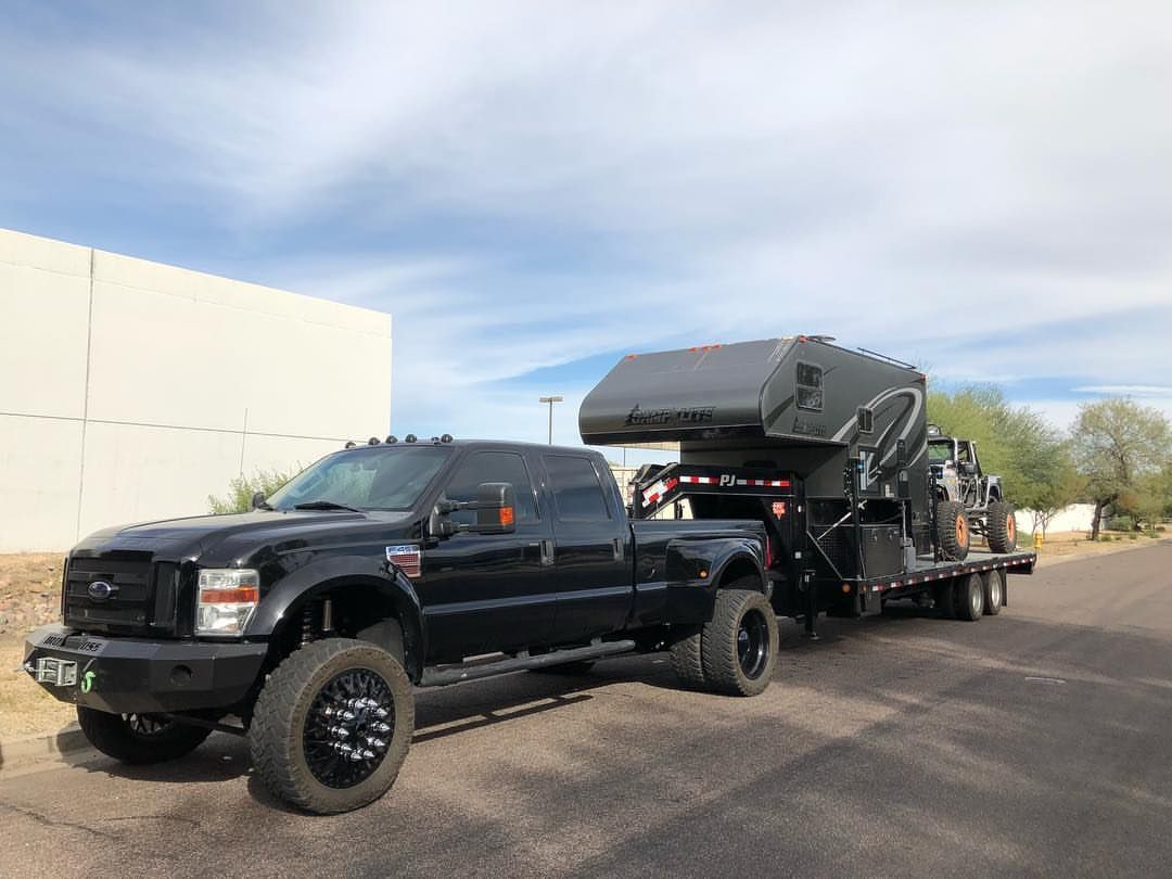 A black truck with a trailer attached to it is parked on the side of the road.