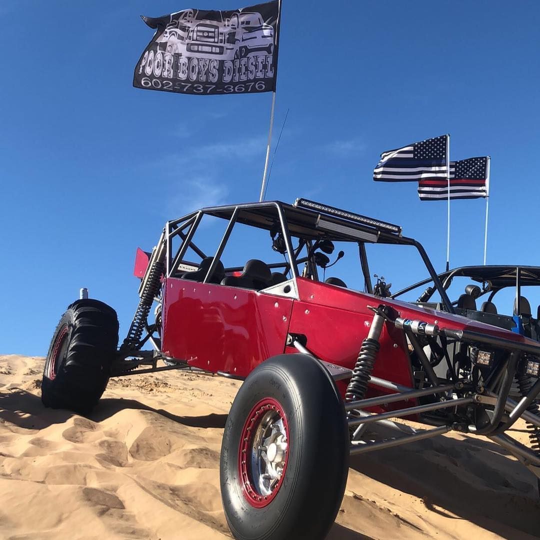 A red buggy is parked on top of a sand dune