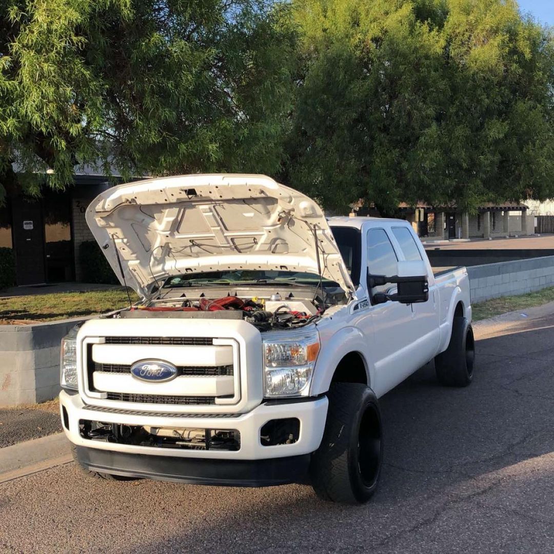 A white truck with the hood up is parked on the side of the road.