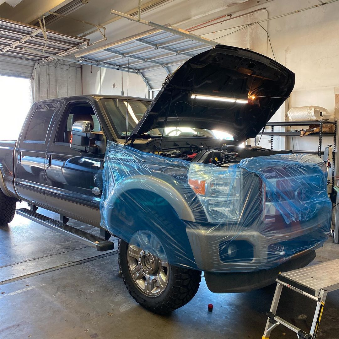 A truck is wrapped in plastic and has its hood open in a garage.