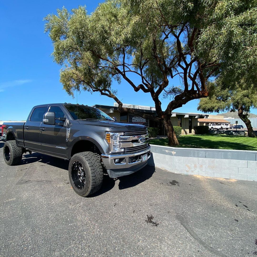 A gray truck is parked in a parking lot next to a tree.