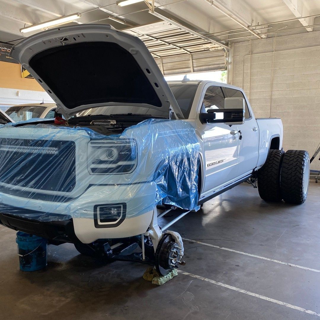 A truck with the hood up is wrapped in plastic in a garage.