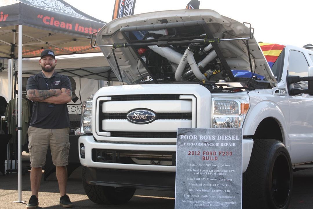 A man is standing in front of a ford truck with the hood open.