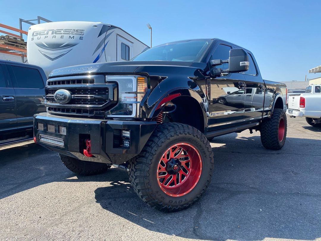 A black truck with red wheels and tires is parked in a parking lot.