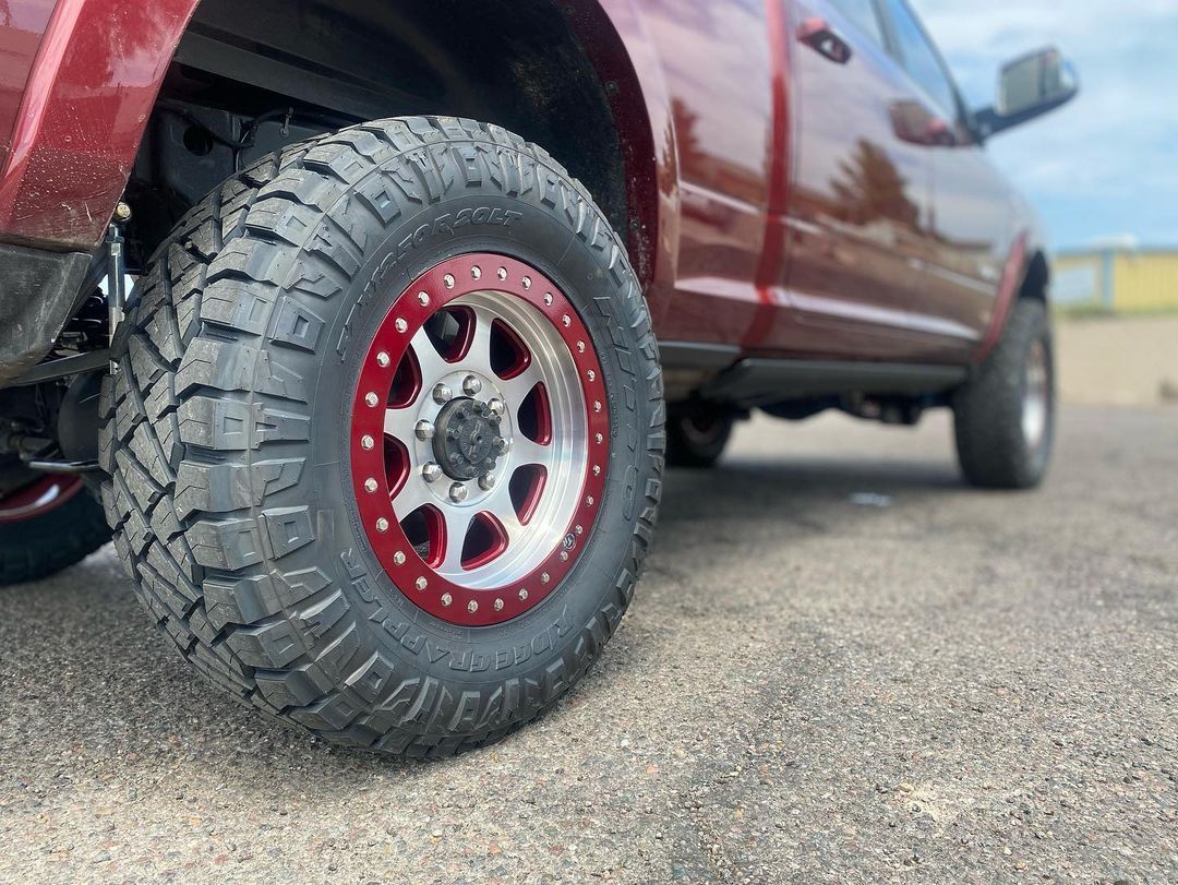 A red truck with red wheels and tires is parked on the side of the road.