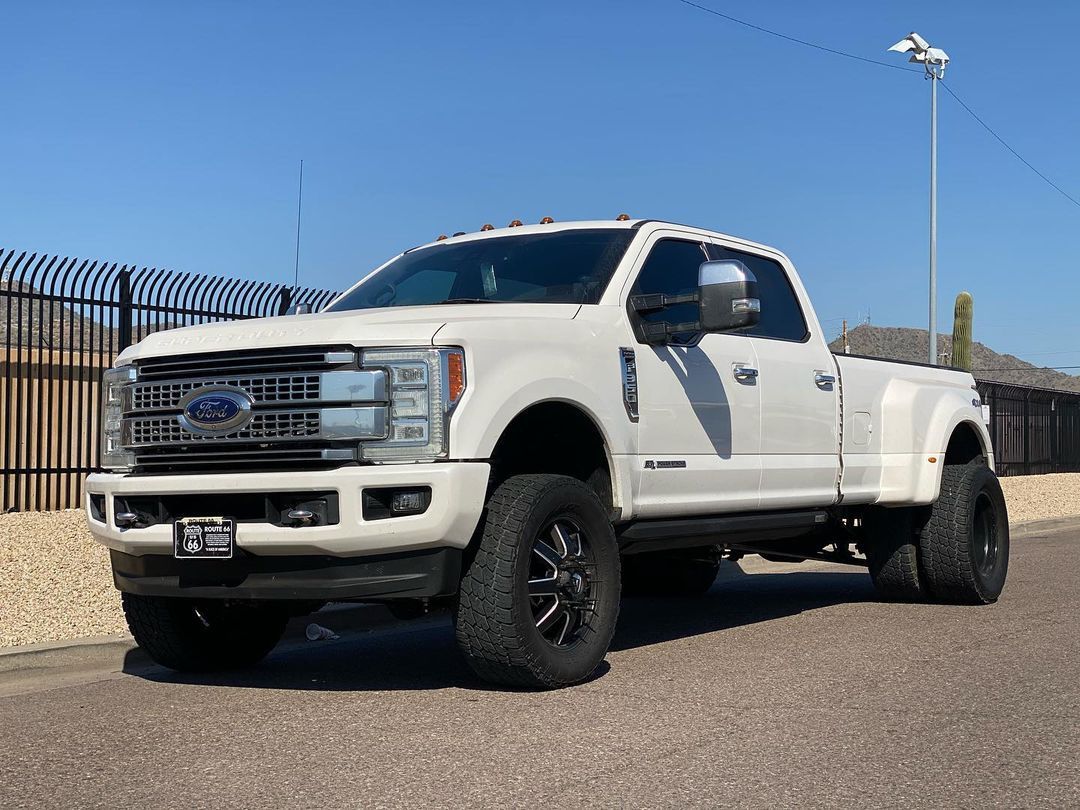 A white ford truck is parked on the side of the road next to a fence.