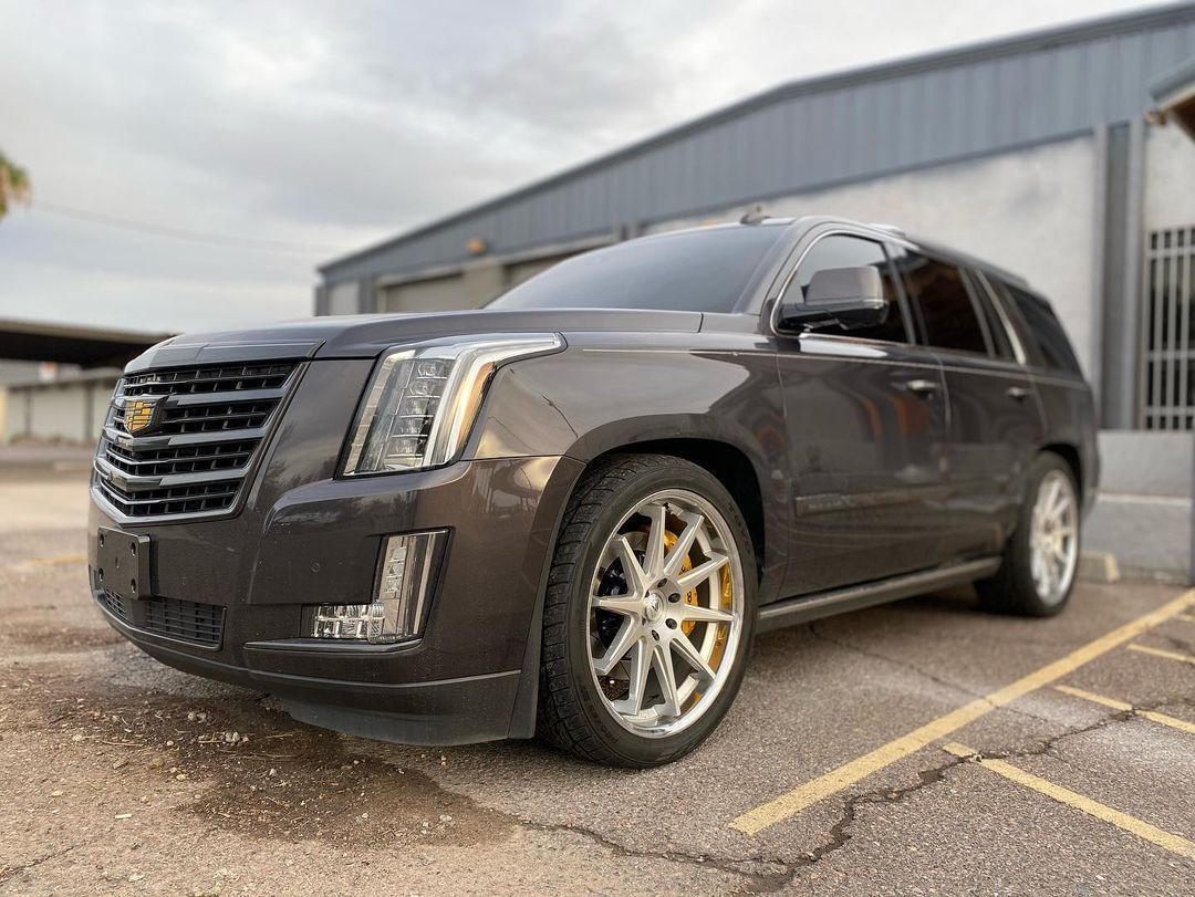 A black cadillac escalade is parked in a parking lot in front of a building.