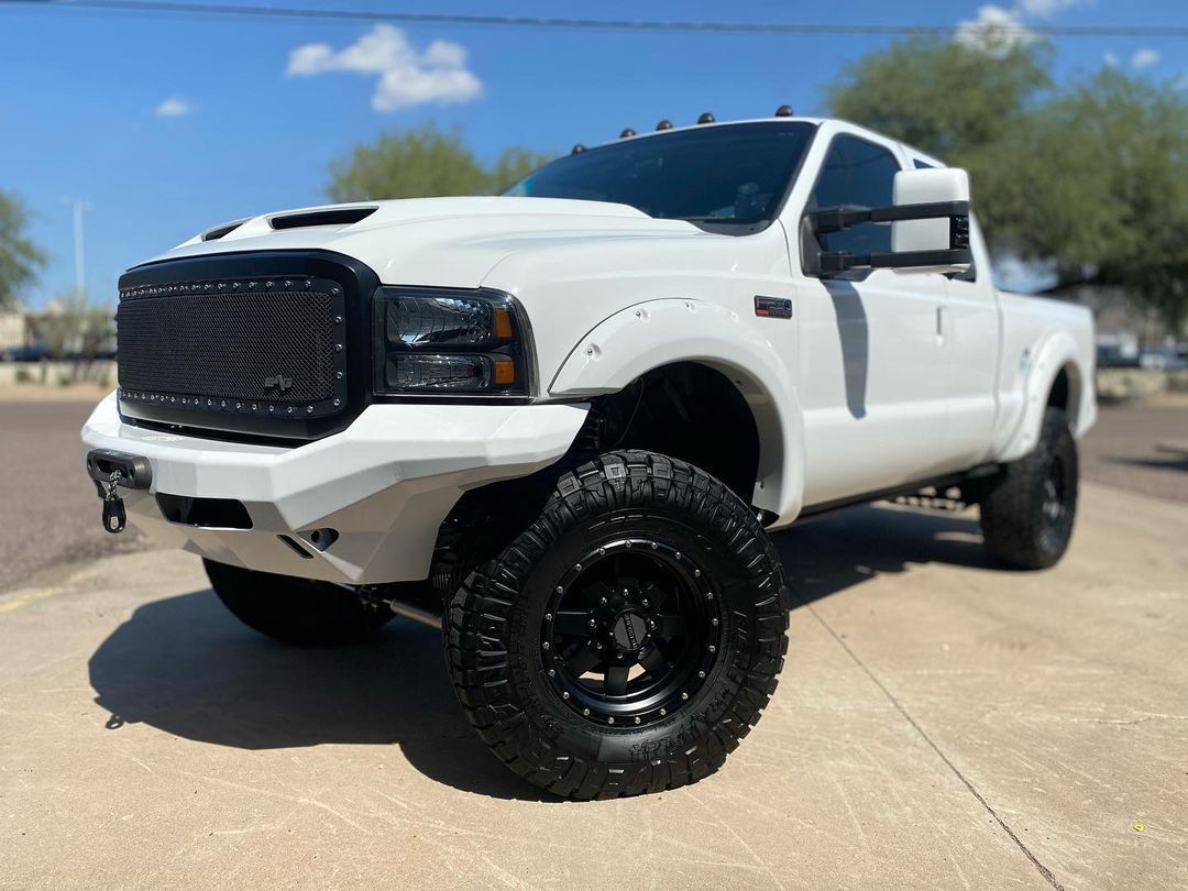 A white truck with black wheels is parked on the side of the road.