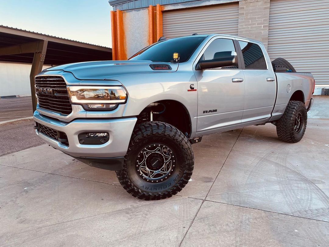 A silver ram truck is parked in a parking lot in front of a building.