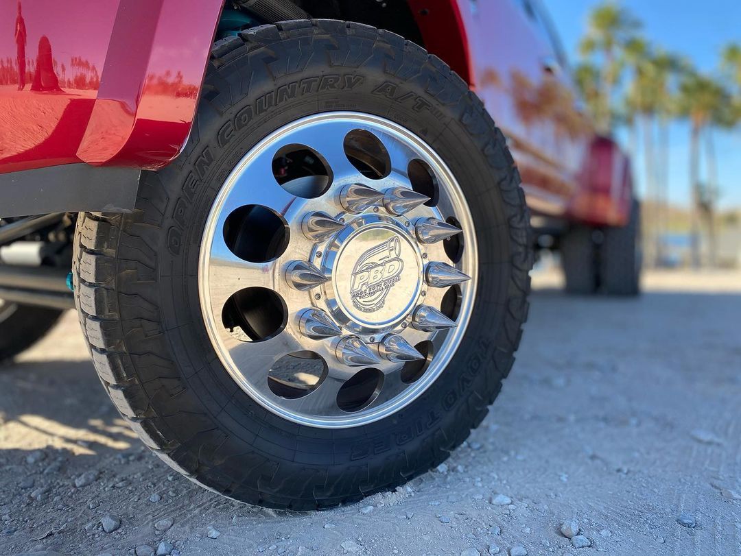 A close up of a red truck 's wheel on a dirt road.