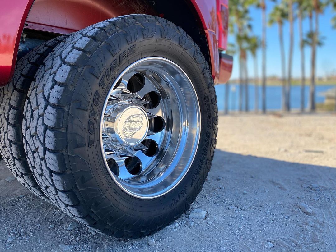 A close up of a tire on a red truck with palm trees in the background.