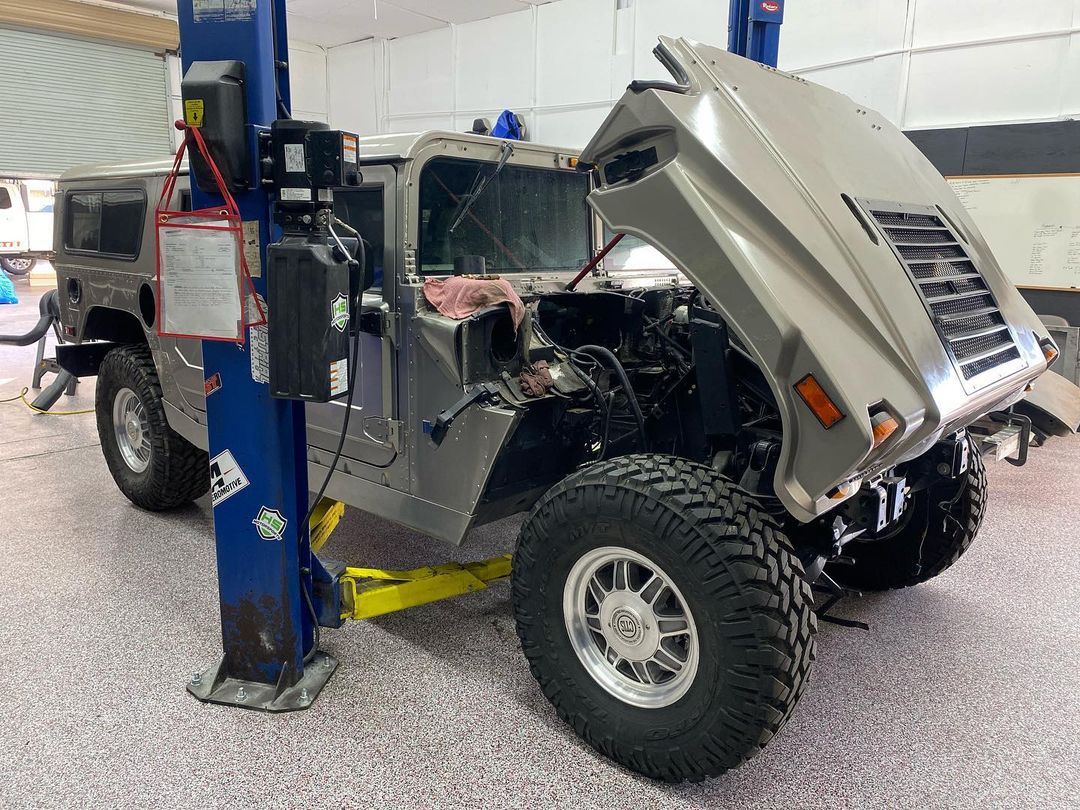 A hummer with the hood up is on a lift in a garage.