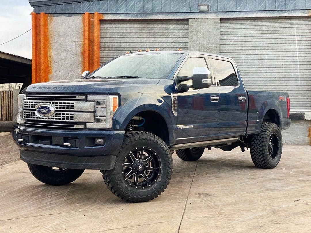 A blue ford f250 pickup truck is parked in front of a building.