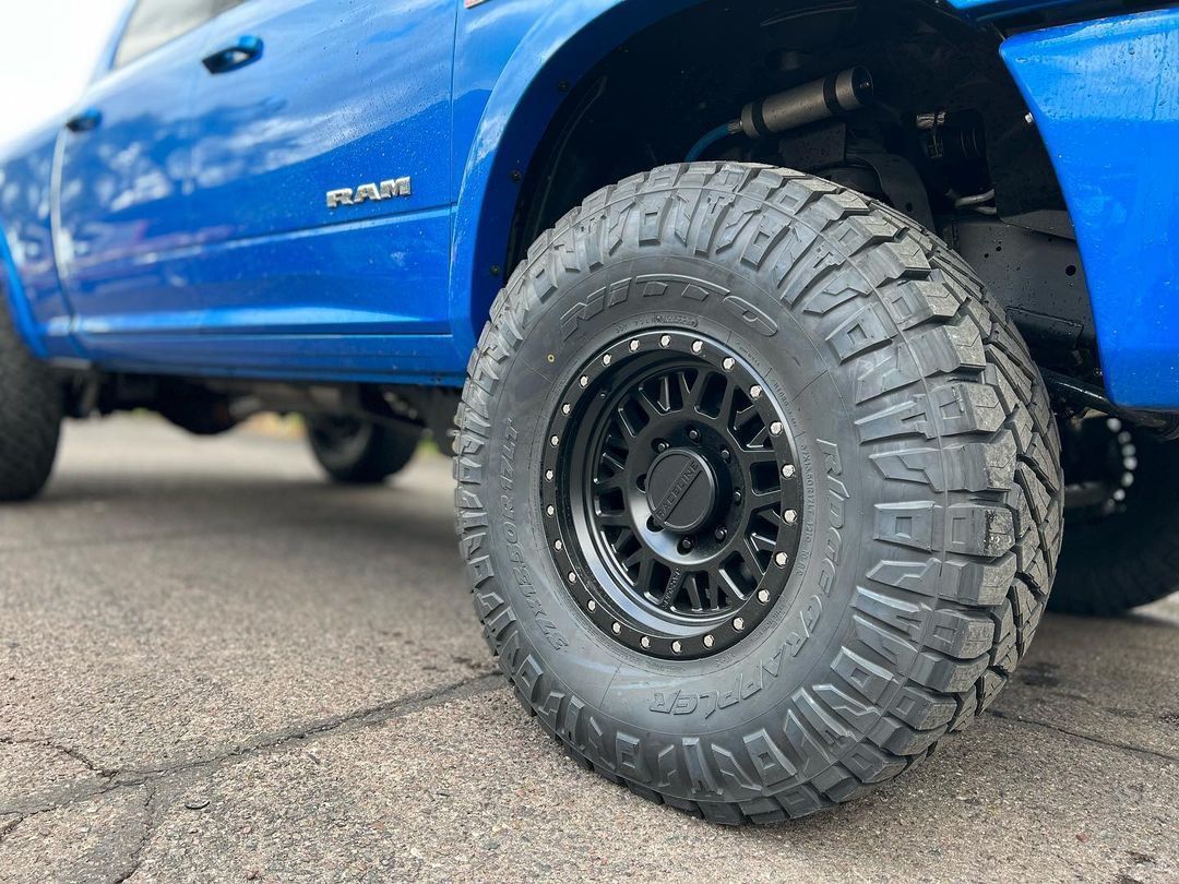 A blue truck with black wheels and tires is parked on the side of the road.