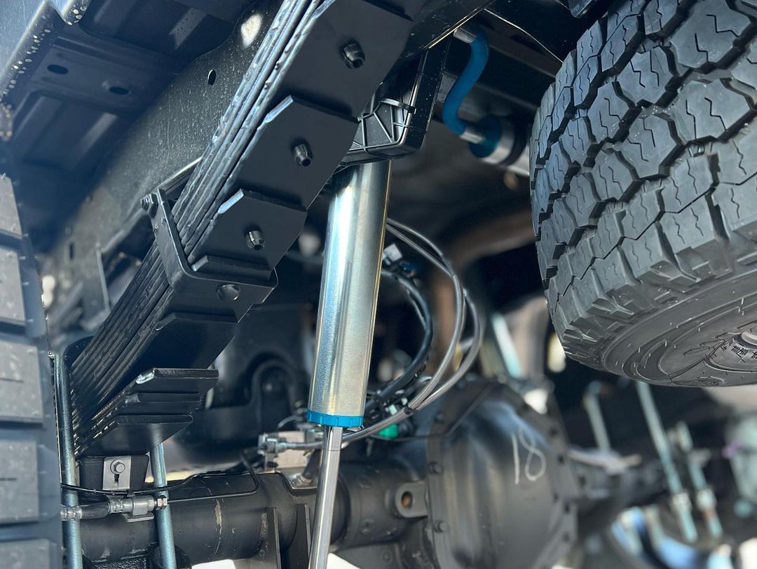 A close up of the underside of a truck with a shock absorber and a tire.