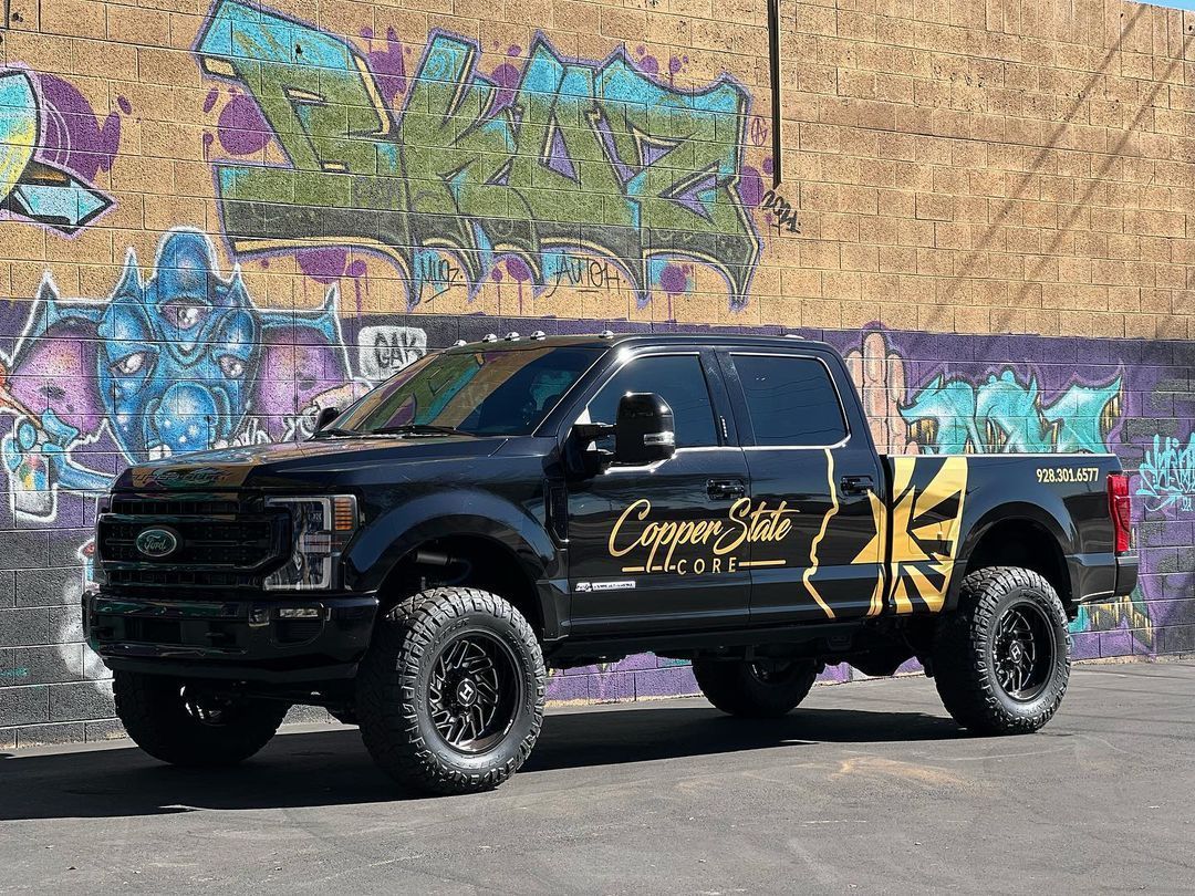 A black truck is parked in front of a graffiti covered wall.