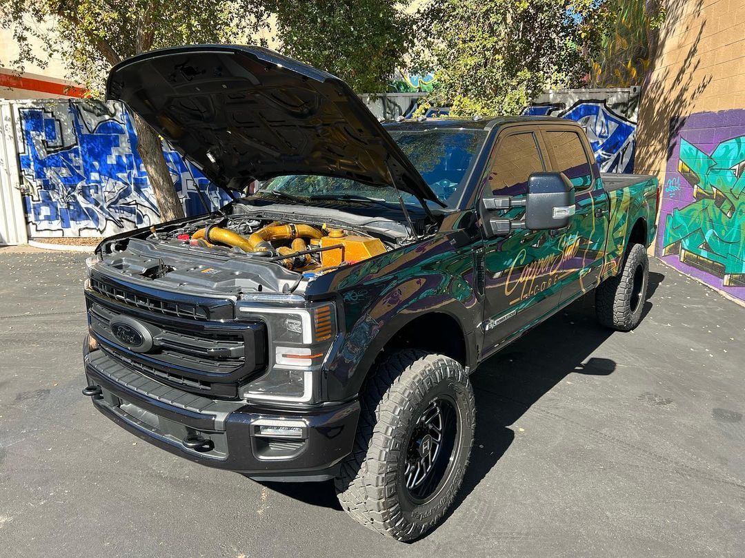 A black truck with the hood up is parked in a parking lot.