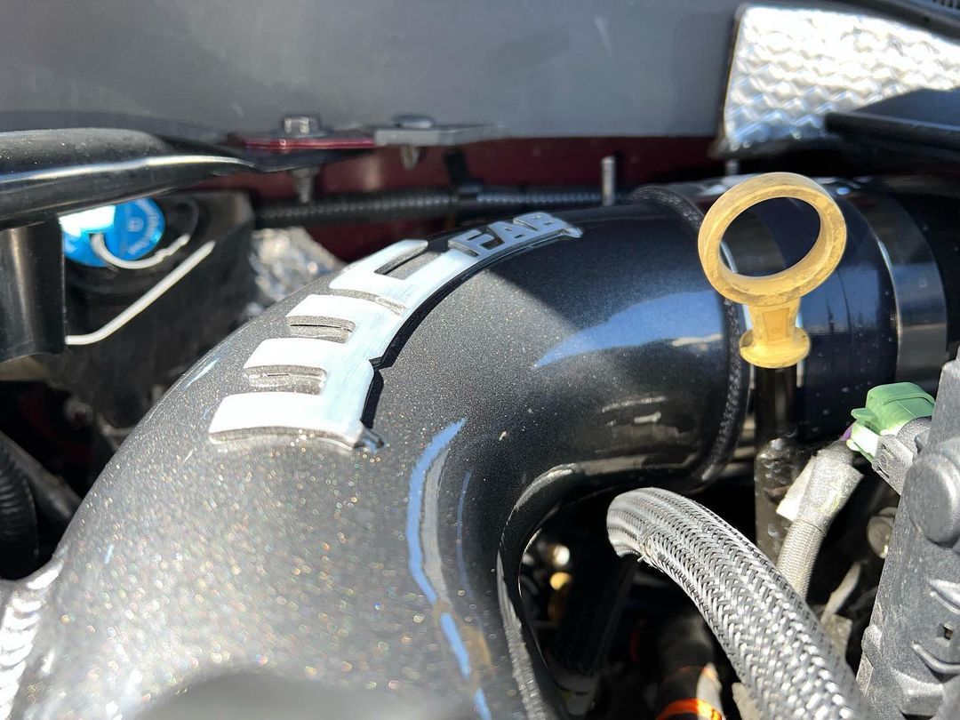 A close up of a car engine with a yellow oil dipstick