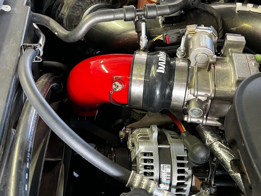 A close up of a car engine with a red hose attached to it.